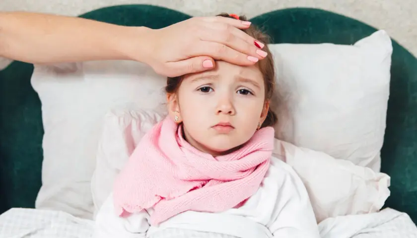 Bambina a letto con sciarpa rosa, mano sulla fronte per controllare la febbre, forse la quarta malattia.