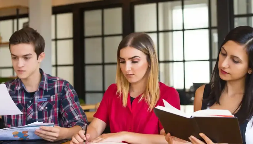 Tre studenti studiano insieme, affrontando parole difficili in inglese. Uno legge un libro, un altro scrive, il terzo analizza documenti.
