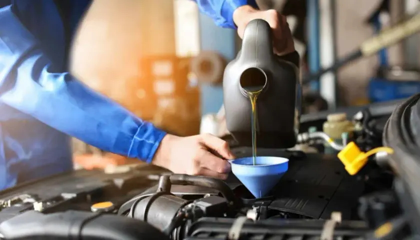 Mechanik w niebieskim kombinezonie wykonuje wymianę oleju w samochodzie, nalewając płyn do silnika przez lejek.