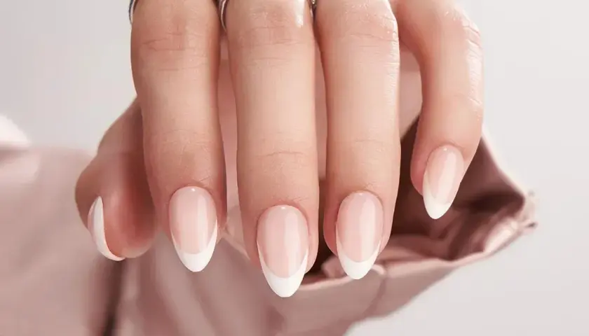 En hand med eleganta, korta french naglar och två glittrande ringar.