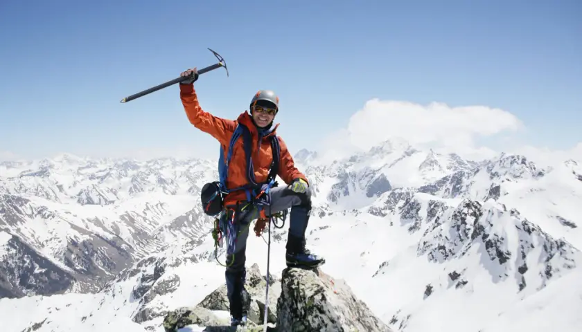 Szczęśliwy alpinista na szczycie, z lodowym toporem w dłoni, podziwia majestatyczne szczyty górskie.