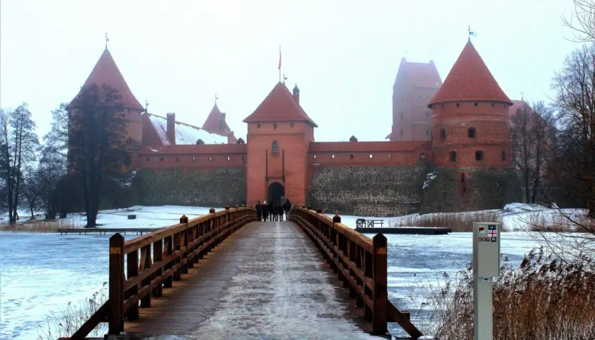 Drewniany most prowadzi do ceglanego zamku w Trokach. Zima otuliła krajobraz śniegiem i lodem.