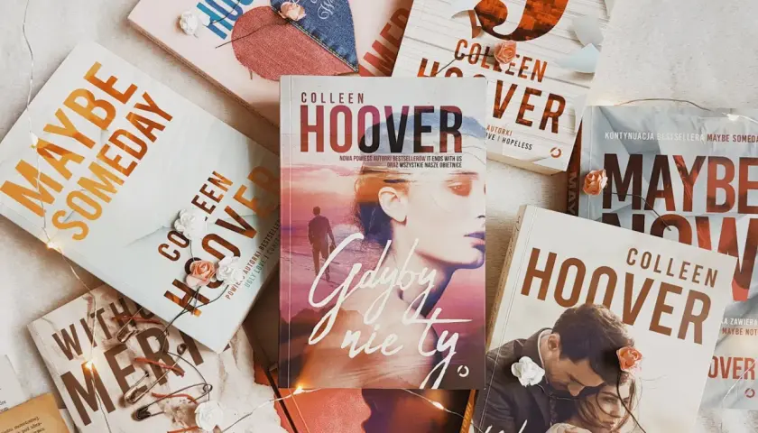 Książki Colleen Hoover ułożone na jasnym tle, ozdobione światełkami i sztucznymi kwiatami. Wśród nich "Gdyby nie ty", "Maybe Someday" i "Wszystkie nasze obietnice".