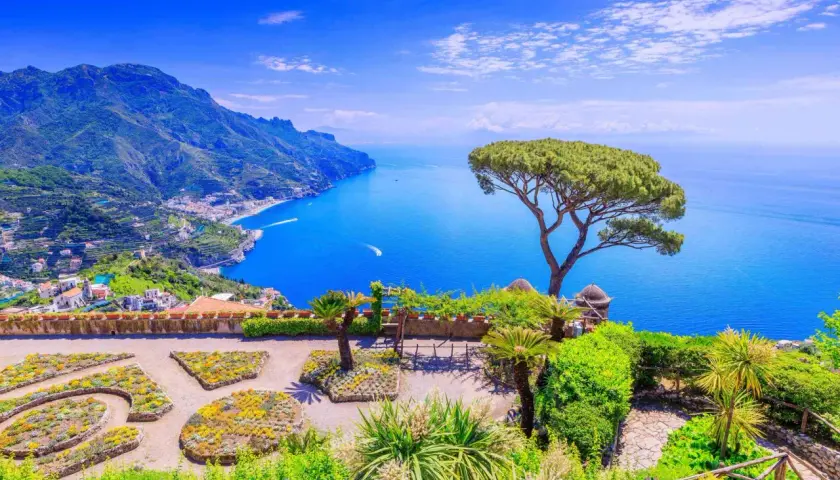 A stunning view of the Amalfi Coast, a perfect destination for a trip from Naples. Lush gardens overlook the sparkling blue sea and dramatic cliffs.