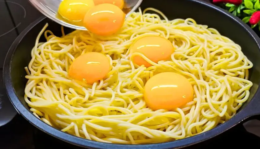 Makaron z jajkiem w patelni, żółtka tworzą złote kropki na żółtym tle.