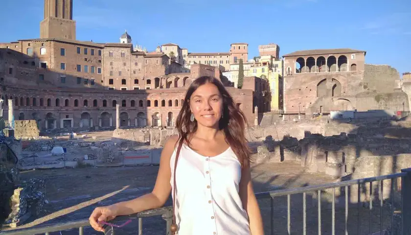 A woman smiles in front of ancient Roman ruins, enjoying a sunny day. This scene suggests that Rome is safe and welcoming for tourists.
