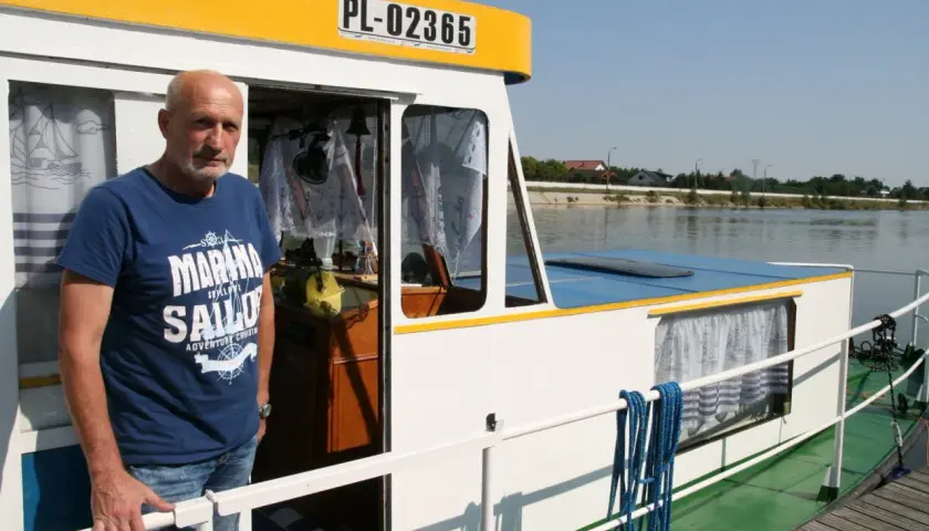 Mężczyzna na pokładzie statku, symbolizującego transport rzeczny. Widoczna tablica rejestracyjna PL-02365.