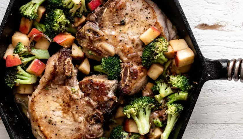 Juicy miso pork chops with roasted broccoli and apple chunks in a cast iron skillet.