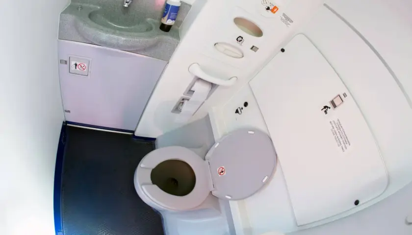 Wnętrze toalety samolotowej z umywalką i otwartą muszlą klozetową.