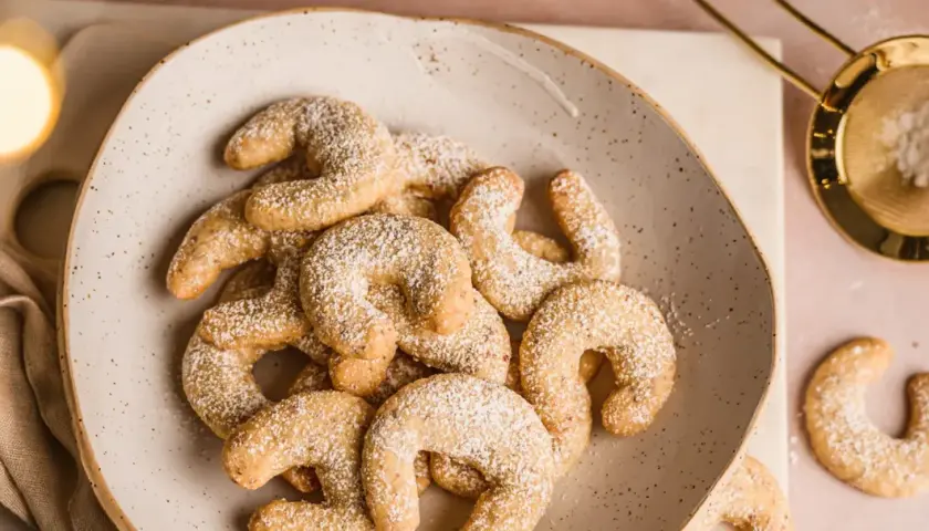 Vanillekipferl low carb, zart bestäubt mit Puderzucker, auf einem rustikalen Teller. Ein Genuss ohne Reue!