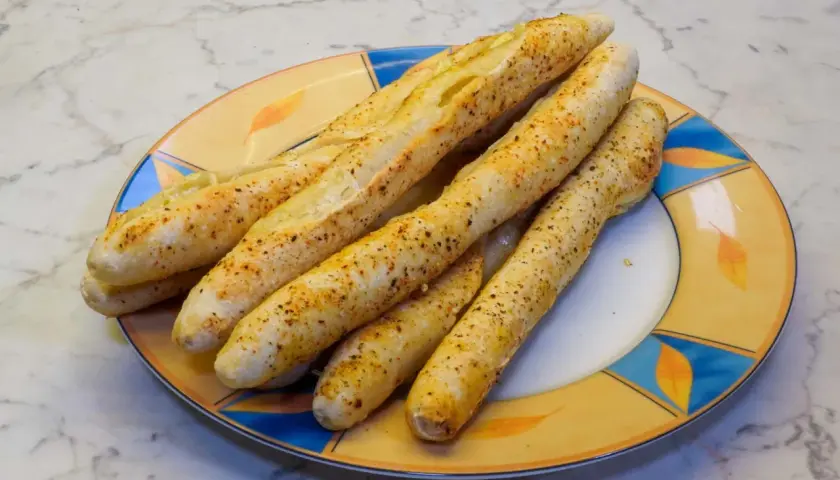 Leckere, knusprige brotstangen aus pizzateig, bestreut mit Gewürzen, liegen auf einem bunten Teller.