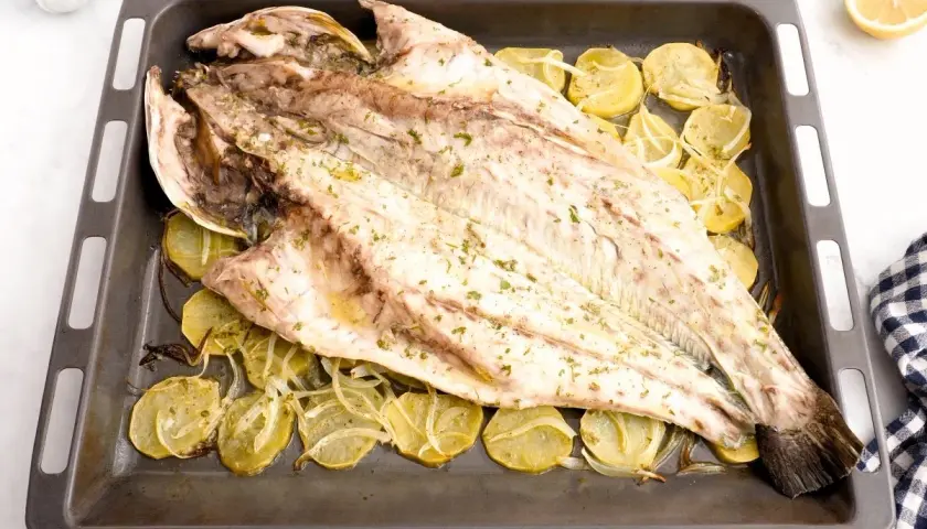 Corvina entera asada con patatas y limón en una bandeja. Una deliciosa opción para tus recetas de corvina.
