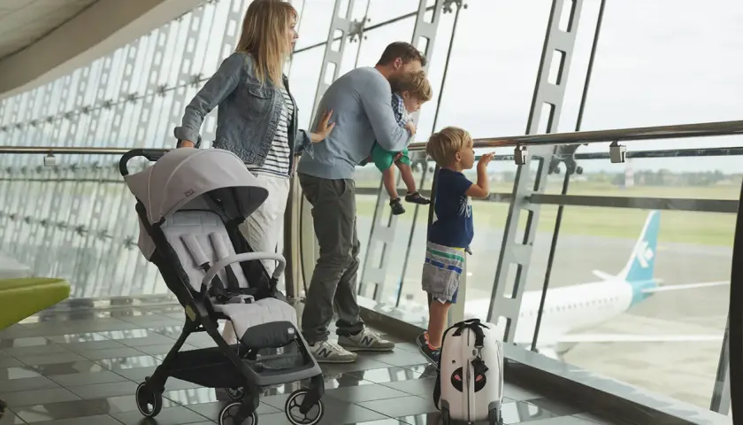 Famiglia in aeroporto, con passeggino e valigia, guarda un aereo. Speriamo che i bambini non soffrano di mal d'aereo!