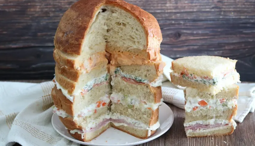 Un monumentale pane gastronomico a più strati, farcito con salmone, verdure e salse cremose, accanto a una versione più piccola.