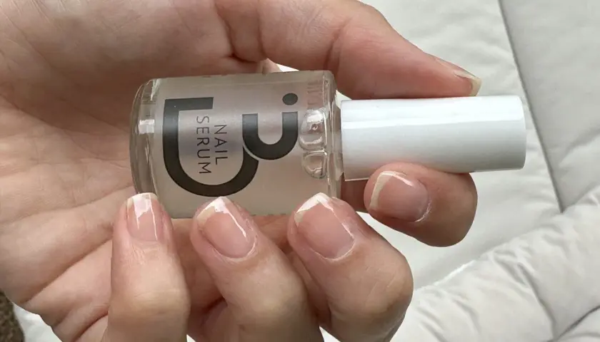 En hand håller en flaska nagelserum. Naglarna ser naturligt starkare och glansiga ut.
