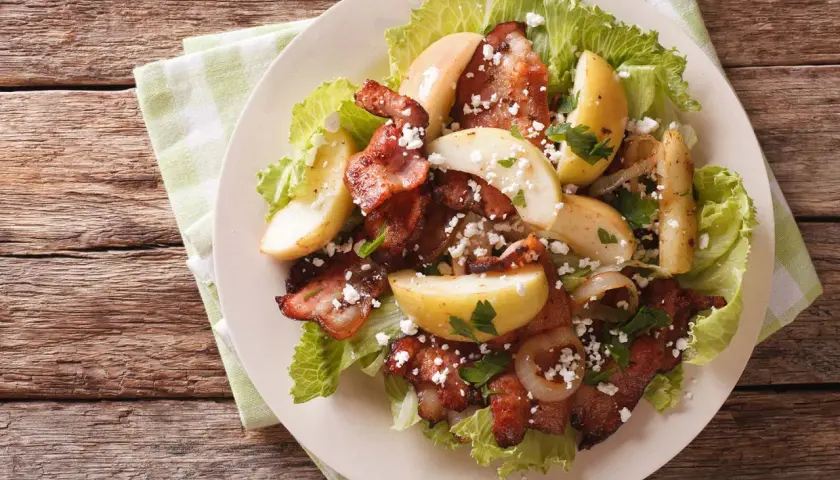 Une délicieuse idée de salade composée : lard croustillant, pommes de terre rôties, oignons caramélisés et fromage émietté sur un lit de laitue.