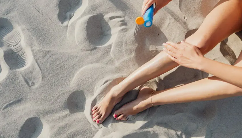 Kobieta smaruje nogi kremem z filtrem zawierającym ethylhexyl methoxycinnamate na piaszczystej plaży.