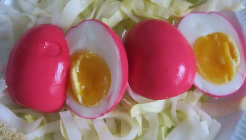 Trois œufs durs à la coquille rose vif, dont deux coupés révèlent un jaune d'œuf coulant, servis sur un lit de chou blanc émincé.