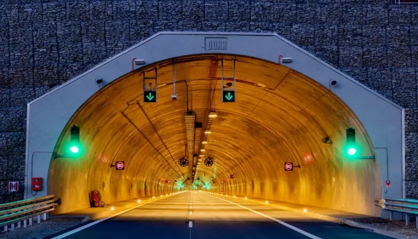 Wjazd do tunelu z kamienną górą w tle. Zielone światła sygnalizacyjne i znaki ograniczenia prędkości 80 km/h.