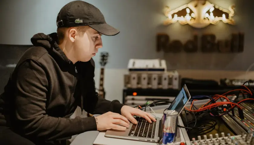 Un jeune beatmaker français concentré sur son ordinateur portable dans un studio d'enregistrement, une canette Red Bull à portée de main.