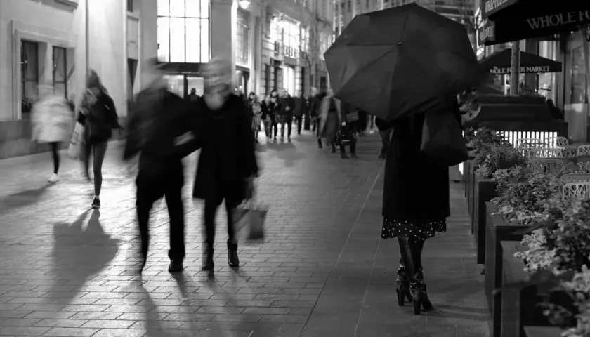 Nocne street photography. Rozmyte postacie spieszą się ulicą, jedna osoba z parasolką.