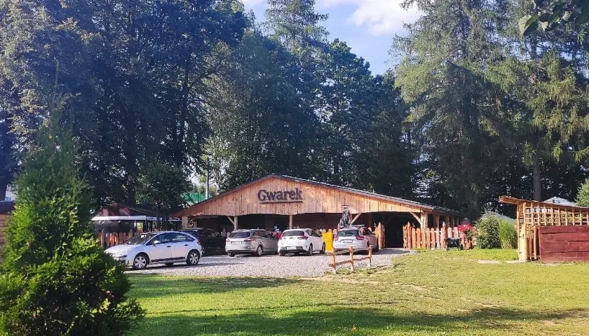 Drewniana restauracja Gwarek w Polańczyku, otoczona zielenią, z zaparkowanymi samochodami.