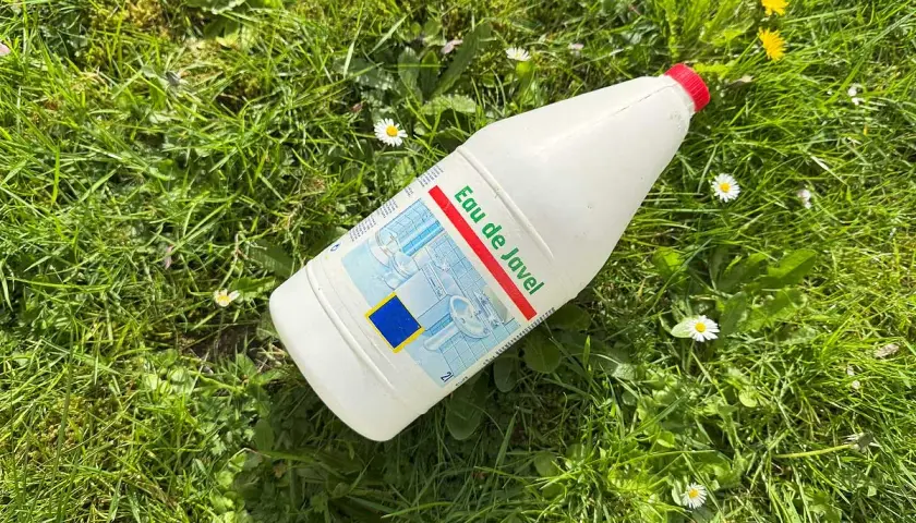 Bouteille d'eau de Javel posée dans l'herbe, parmi des pâquerettes. Un désherbant maison qui peut aussi servir pour le ménage.