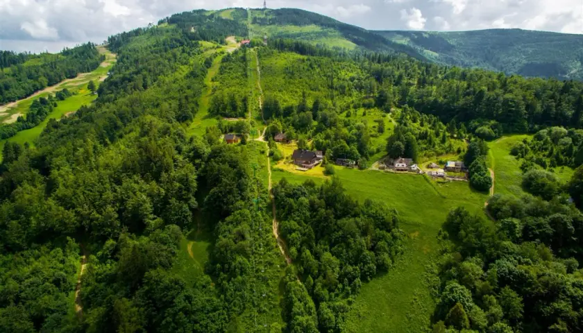 Widok z lotu ptaka na zielone zbocza Skrzycznego z kolejką linową i domkami.
