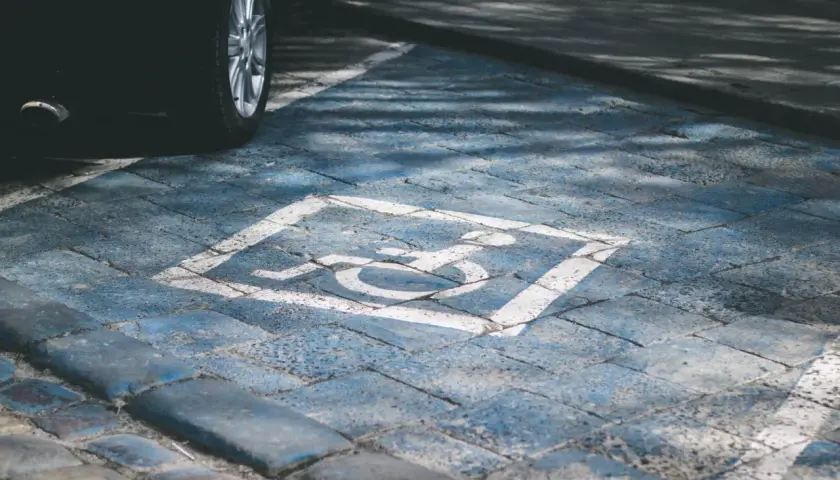 Wyznaczone miejsce parkingowe dla niepełnosprawnych pod blokiem. Symbol wózka inwalidzkiego na niebieskim tle.