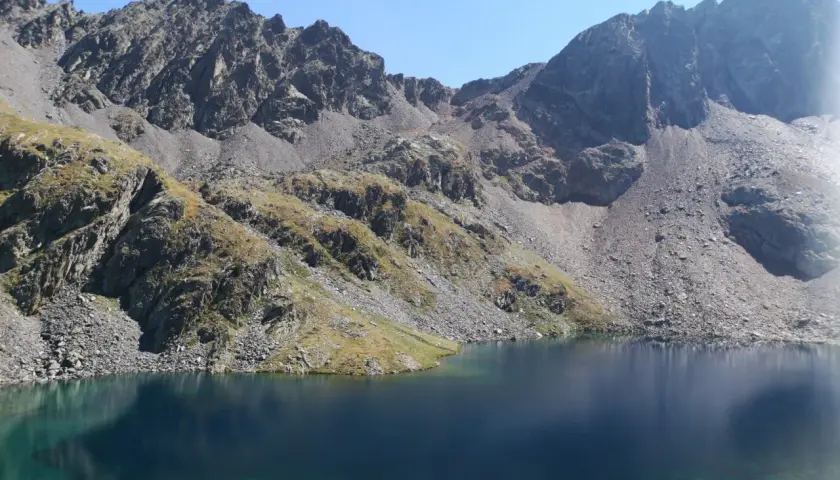 Lago sereno y montañas rocosas cerca del refugi de Baiau.