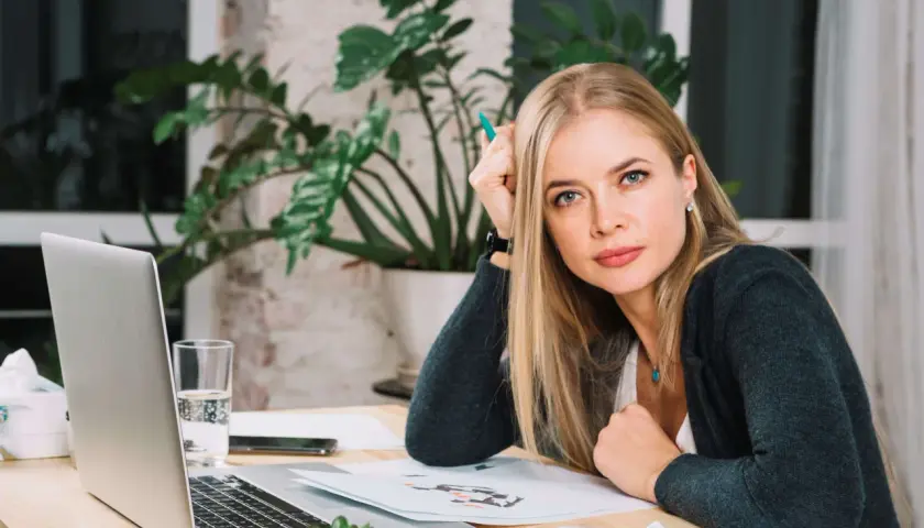 Blondynka z zielonym długopisem w dłoni, zastanawia się nad różnymi rodzajami odpoczynku, siedząc przy biurku z laptopem.