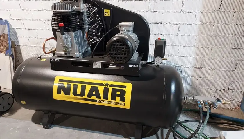 Un compresor de uña NUAIR, negro, con etiqueta amarilla y detalles plateados. Ideal para tu taller.