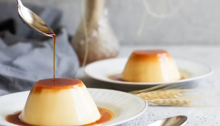 Delicioso flan de huevo con caramelo líquido cayendo de una cuchara. Una receta casera que enamora.