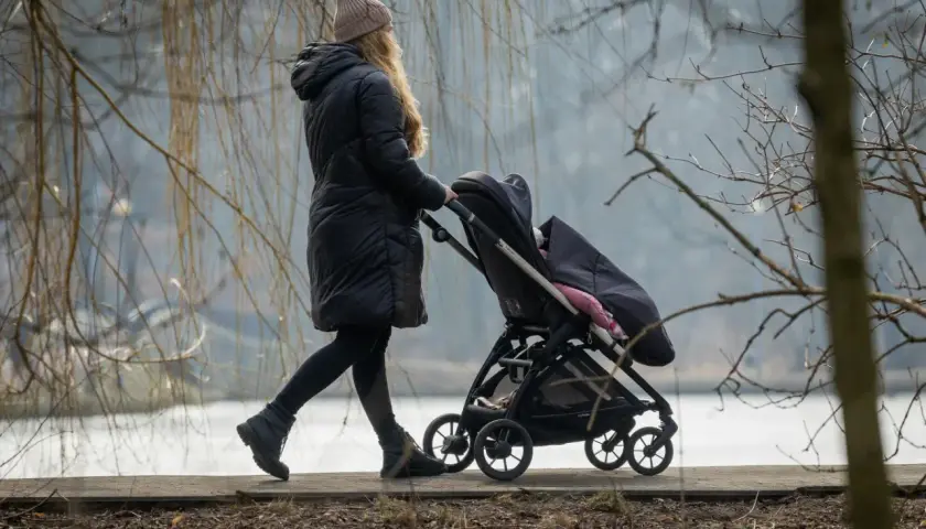 Kobieta na urlopie macierzyńskim spaceruje z dzieckiem w wózku. Zastanawia się, urlop macierzyński ile płatny, by zapewnić dziecku wszystko, co najlepsze.