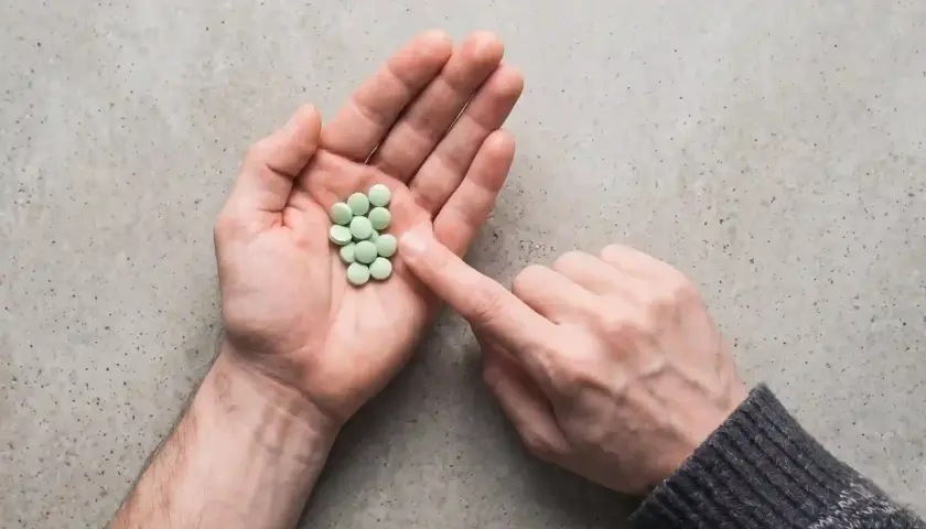 Mano aperta con un mucchietto di pillole verdi, come un trittico gocce. Un dito le indica.