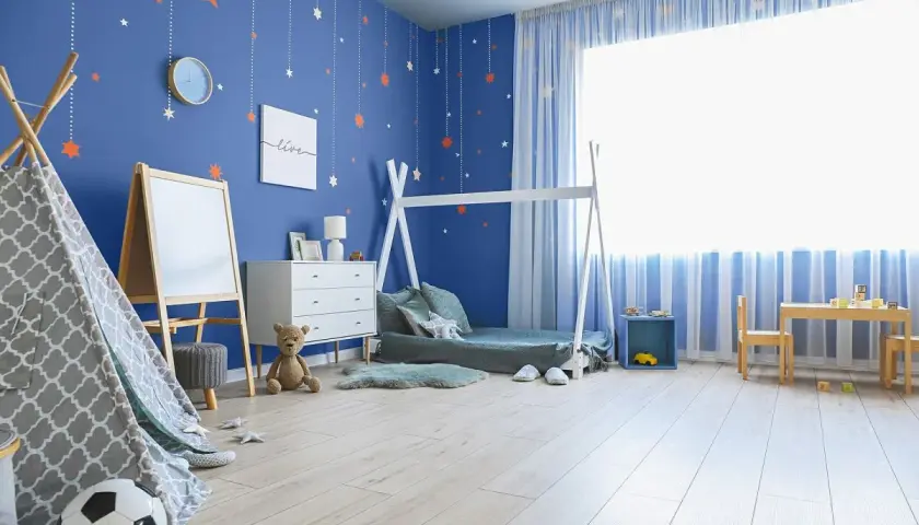 Niebieskie kolory ścian w pokoju chłopca ozdobione wiszącymi gwiazdkami tworzą magiczną atmosferę.