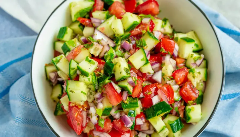 Frischer Tomaten-Gurken-Salat mit roten Zwiebeln und Kräutern, serviert in einer Schüssel.