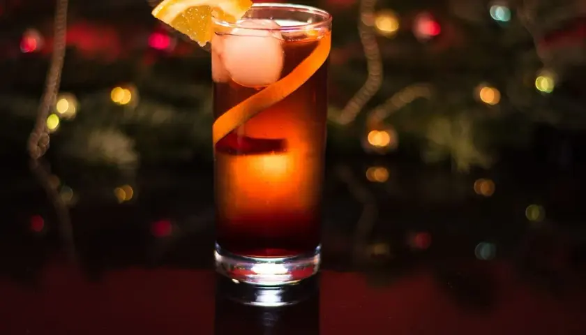 Elegancki drink z campari, lodem i pomarańczą, na tle świątecznych światełek.