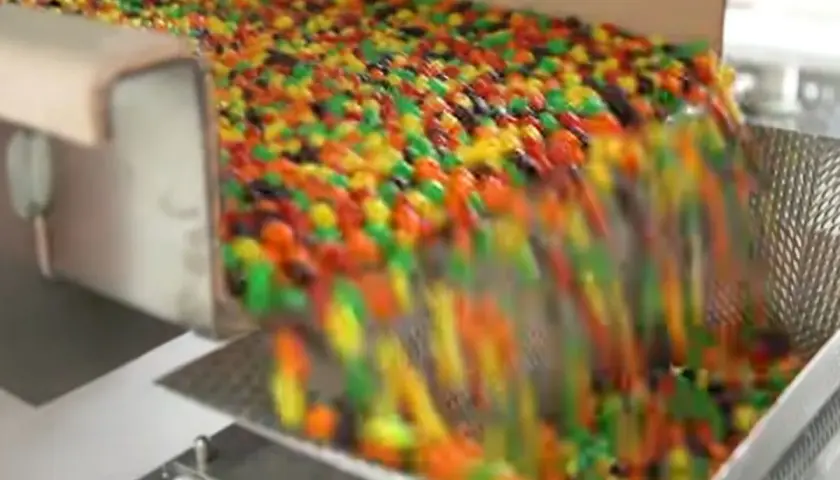 Kolorowe drażetki spadają z taśmociągu. Czy skittles są bezglutenowe? To pytanie nurtuje wielu łasuchów.