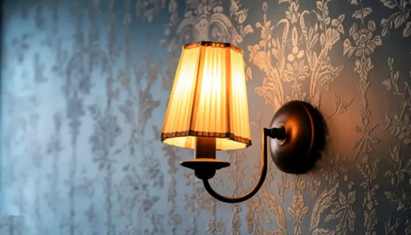 Aplique de pared rústico con pantalla plisada iluminada sobre papel tapiz floral.