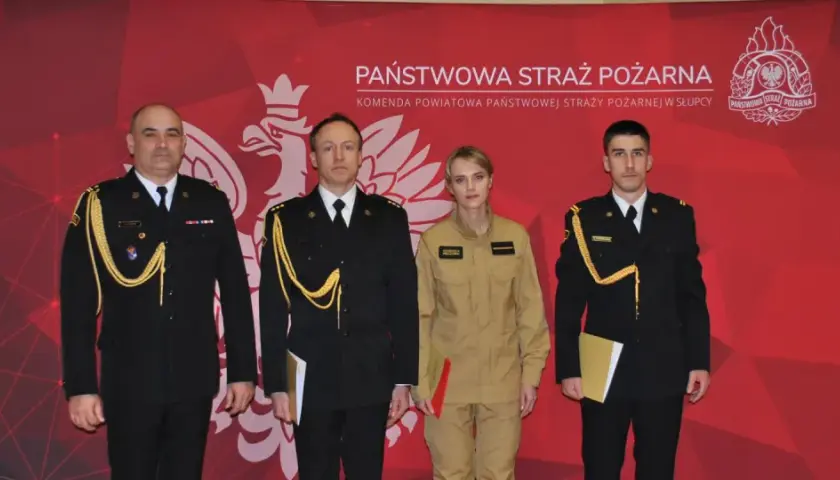 Czterech funkcjonariuszy Państwowej Straży Pożarnej w galowych mundurach i kombinezonie, z odznaczeniami i dokumentami.