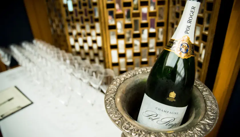 Bouteille de champagne Pol Roger dans un seau à glace, avec des flûtes alignées en arrière-plan.