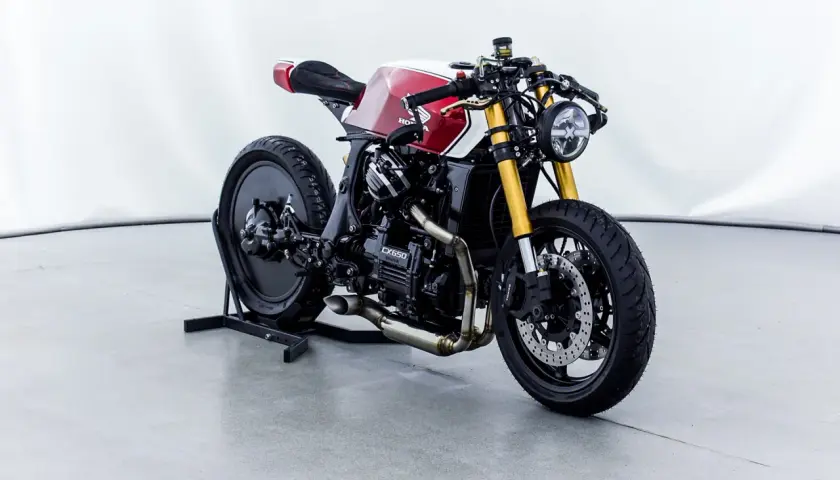 Honda CX650 custom cafe racer, rossa e bianca, con forcella dorata e scarico modificato. Un vero gioiello su due ruote.