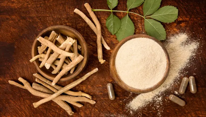 Ashwagandha roots, powder, and capsules on a wooden surface with leaves.