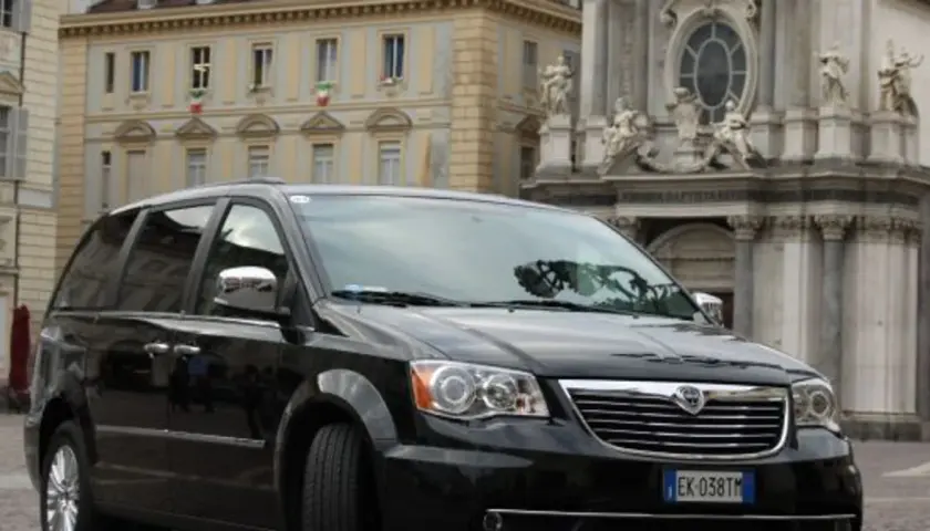 Czarny Lancia Voyager na tle zabytkowej architektury.