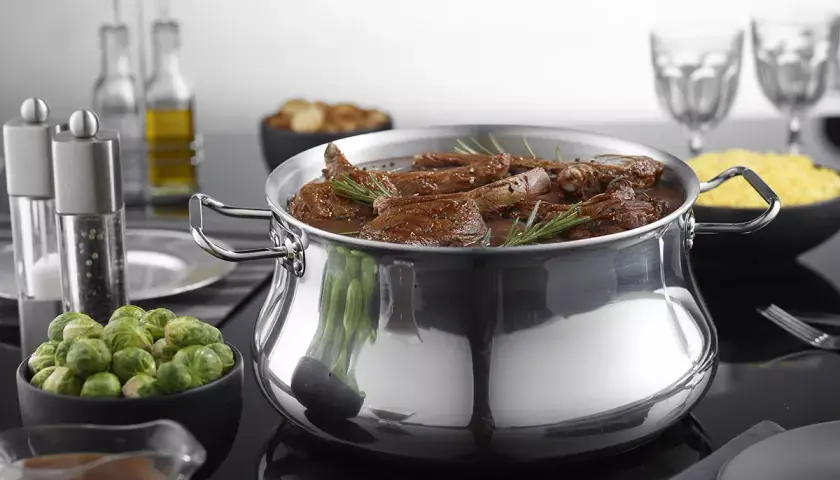 Un plat mijoté dans une cocotte en aluminium brillant, prêt pour le nettoyage. Des accompagnements comme des choux de Bruxelles et du riz sont disposés autour.