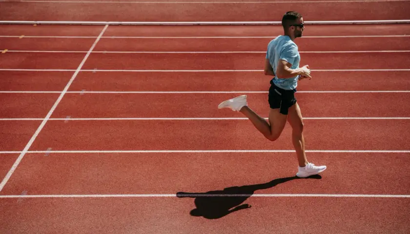 Mężczyzna w niebieskiej koszulce i czarnych spodenkach biegnie po bieżni lekkoatletycznej.