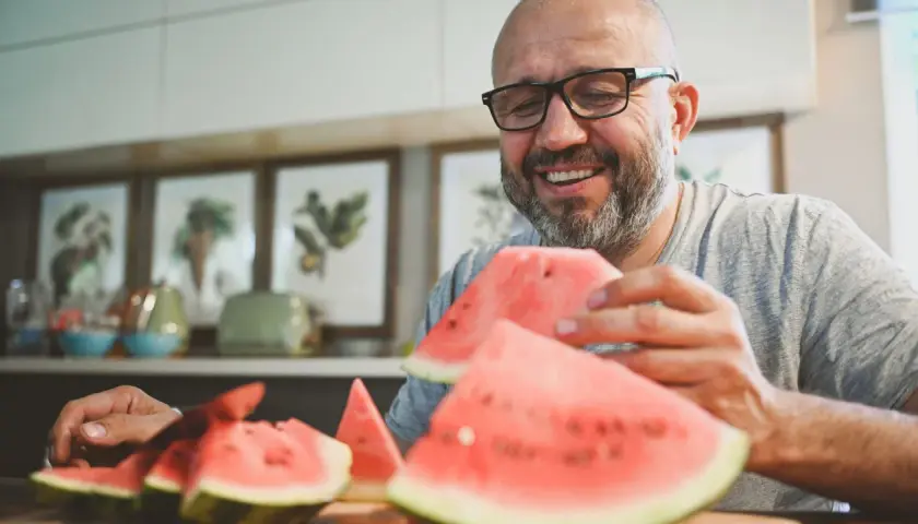 Glücklicher Mann mit Brille isst Wassermelone. Wenige kalorien Wassermelone ist ein gesunder Snack.