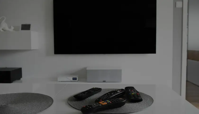 Na stole leżą piloty, a czarny ekran telewizora sugeruje, że jest brak obrazu.