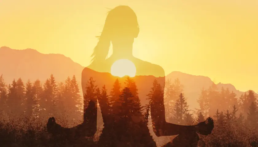 Silhouette di donna in meditazione con tramonto e foreste. Un'immagine che ispira a come ridurre lo stress con la natura.